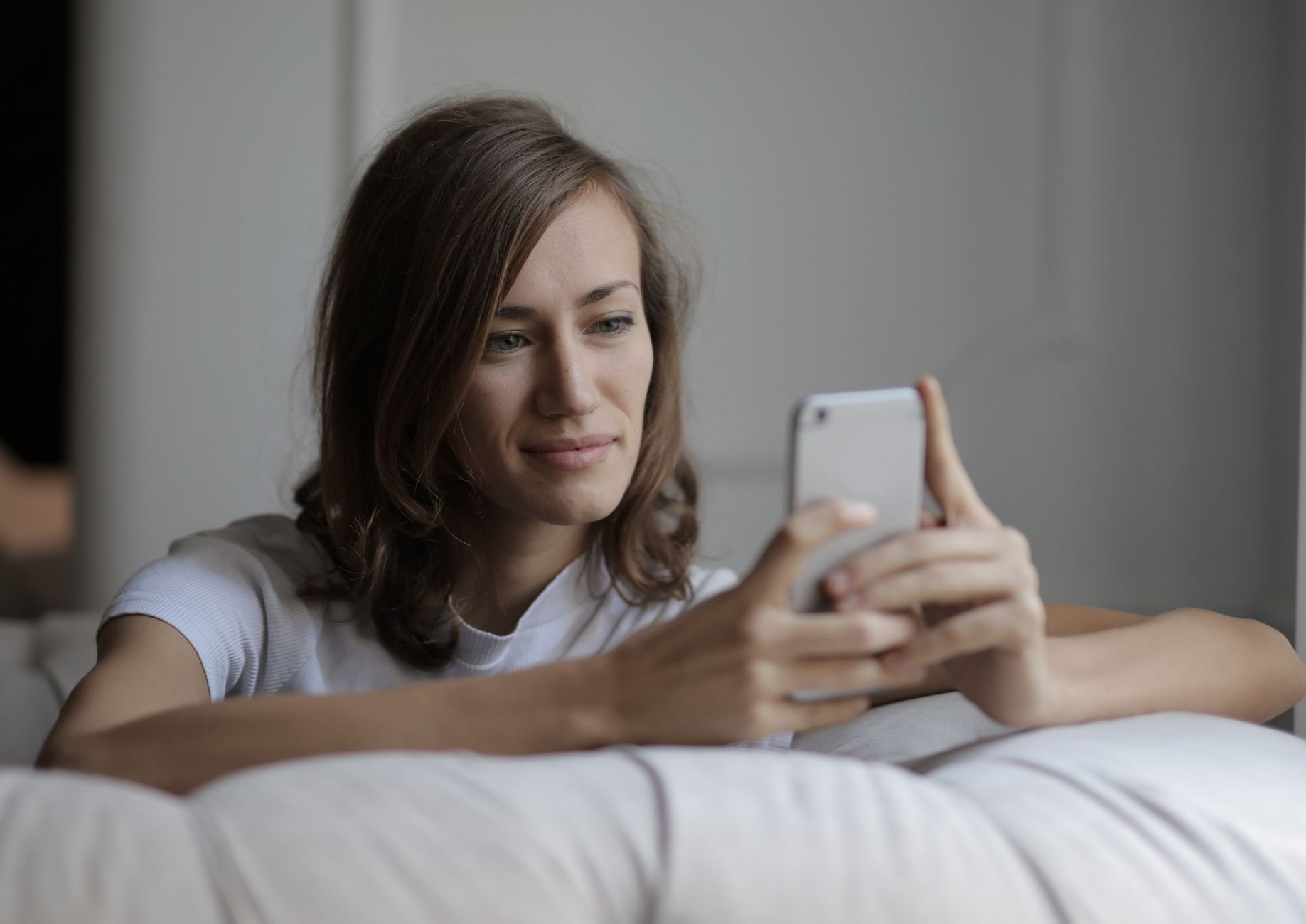 Woman smiling while relaxing on a couch, using her smartphone